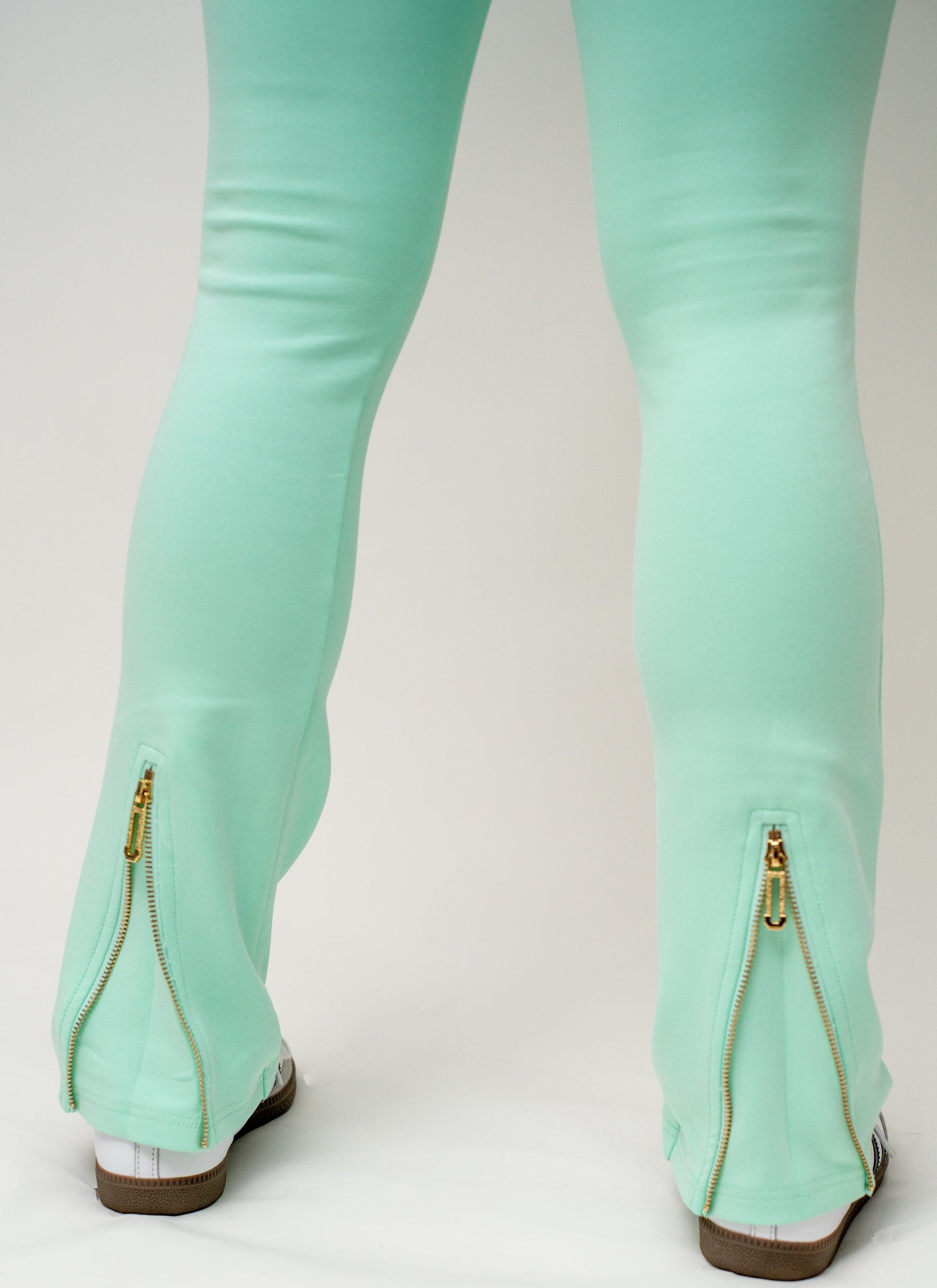 Mint green leggings with gold zippers on a white background