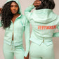 Person wearing a mint green tracksuit with 'VERYWHERE' text on the back against a beige background